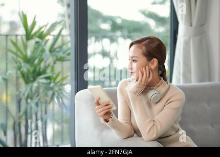 Glückliche asiatische junge Frau entspannen sich auf dem Sofa zu Hause verloren In Gedanken träumen oder planen Stockfoto