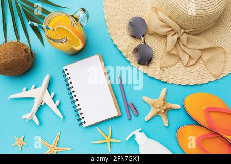 Notizblock mit Textplatz neben einem Spielzeugflugzeug und diversen Accessoires zur Entspannung auf blauem Hintergrund, sommerlicher Hintergrund. Stockfoto