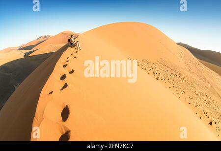 Einsamer Mann, der auf Sand in der Dune 45 in Sossusvlei sitzt - Konzept der Fernweh in namibischer berühmter Wüste - Abenteuer Reise nach african Wonders Stockfoto