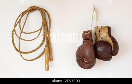 Die alten Boxhandschuhe mit Springseil hängen an einem Weiße Wand Stockfoto