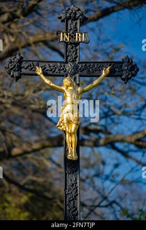 Ein eisernes Kreuz mit dem gekreuzigten Jesus Christus auf einem Hintergrund Bäume und von blauem Himmel Stockfoto