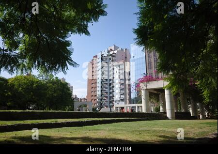 Üppiges Laub und Rasen im öffentlichen Park namens Plaza Italia in Cordoba. Moderne Wohngebäude aus Glas und Beton in der 27 de Abril Stockfoto