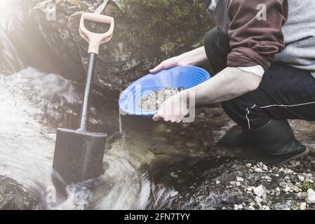 Outdoor-Abenteuer auf dem Fluss. Goldwaschen, nach Gold suchen. Der Mann sucht Gold mit einer Goldpfanne in einem kleinen Bach Stockfoto