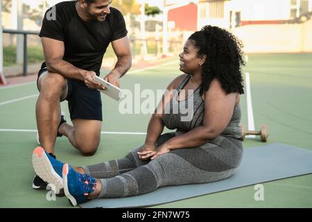 Personal Trainer arbeitet mit kurvigen Frau, während sie ihre Konstruktion Mit digitalem Tablet während des Trainings - Sport People Lifestyle Konzept Stockfoto