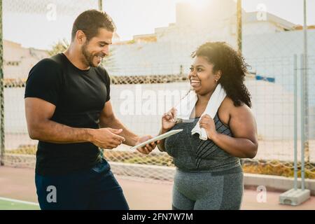 Personal Trainer arbeitet mit kurvigen Frau, während sie ihre Konstruktion Mit digitalem Tablet während des Trainings - Sport People Lifestyle Konzept Stockfoto