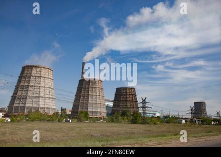 Pavlodar-Wärmekraftwerk. Kühltürme und Rauchschwaden mit weißem Rauch. Grünes Gras, blauer Himmel mit Wolken. Stockfoto