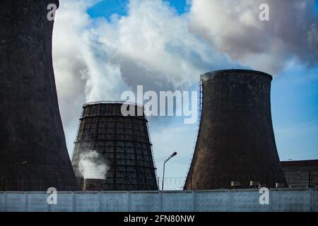 Nahaufnahme des thermischen Kraftwerks Pavlodar. Alte und neue Kühltürme mit weißem Rauch. Blauer Himmel mit Wolken. Stockfoto