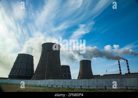 Silhouette Blick auf das thermische Kraftwerk Pavlodar. Kühltürme links. Rauchstapel mit weißem Rauch rechts. Blauer Himmel mit Wolken. Stockfoto