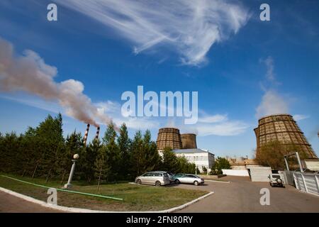 Pavlodar-Wärmekraftwerk. Kühltürme und Rauchschwaden mit weißem Rauch. Grünes Gras, Bäume, blauer Himmel mit Wolken. Stockfoto