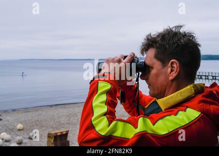 15. Mai 2021, Schleswig-Holstein, Eckernförde: DLRG-Mitarbeiter Björn Fischer schaut durch das Fernglas. Die ersten Stationen der Deutschen Rettungsgesellschaft (DLRG) an der Nord- und Ostsee werden derzeit eröffnet. Foto: Frank Molter/dpa Stockfoto