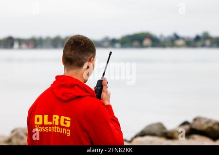 15. Mai 2021, Schleswig-Holstein, Eckernförde: Ein DLRG-Mitarbeiter steht mit einem Radio am Strand. Zur Zeit werden die ersten Stationen der Deutschen Gesellschaft für Lebensrettung (DLRG) an der Nord- und Ostsee eröffnet. Foto: Frank Molter/dpa Stockfoto