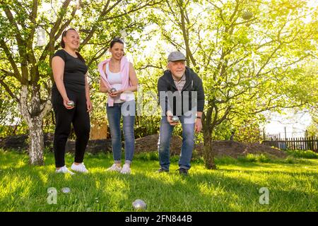 Eine fröhliche, positiv lächelnde Familie, die an einem schönen Sommertag im Garten im traditionellen französischen Petanque-Spiel spielt und die Freizeit genießt Stockfoto