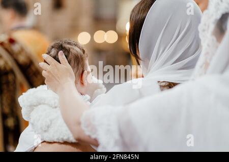 Das Sakrament der Taufe. Mama streichelt das Kind in der Kirche auf den Kopf. Stockfoto