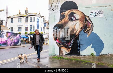 Brighton UK 15. Mai 2021 - dieser Hund rast an einem ziemlich großen Hundegemälde an einem regnerischen Tag in Brighton vorbei, während heute in den meisten Teilen Großbritanniens feuchtes Wetter fegt : Credit Simon Dack / Alamy Live News Stockfoto