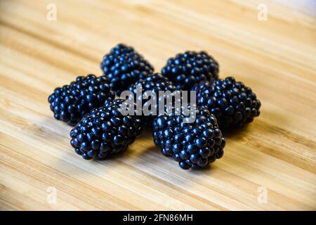 Sieben große reife Brombeeren in Form von Blume auf Holzhintergrund gelegt. Frische Beeren auf Bambusoberfläche, gesundes Lebensmittelkonzept. Nahaufnahme. Stockfoto