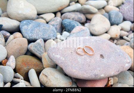 Goldene Eheringe auf Kieselsteinen am Strand. Rustikales Hochzeitskonzept. Stockfoto