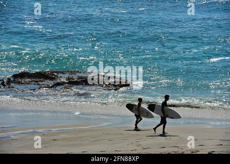 Malerische Küste mit zwei Surfern, die entlang der sandigen Küste des Oceanside Beach in San Diego, Kalifornien, USA, wandern. Stockfoto