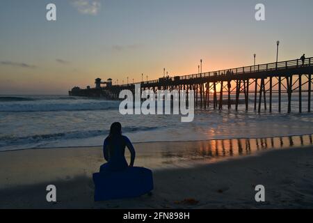 Malerische Sonnenuntergangs-Seeseite mit einem Surfer auf einem Surfbrett mit Blick auf den Oceanside Beach Pier in San Diego Südkalifornien USA. Stockfoto