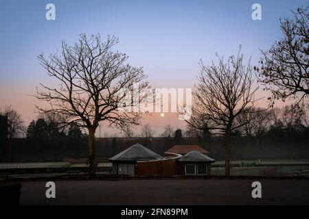 Der Mond über der Westküste Mainline, zwischen zwei Bäumen vom Mesnes Park in Wigan aus gesehen. Stockfoto