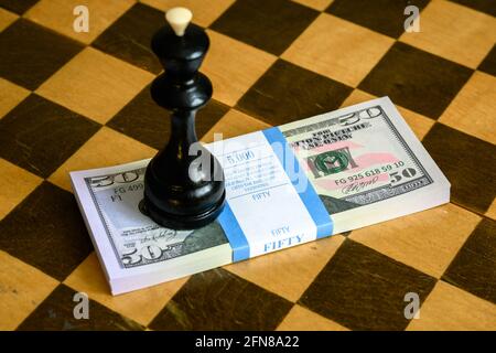Schachkönig und Dollarscheine stapeln sich auf Schachbrett, US-Papierwährung und Spiel. Konzept von Geldstrategie, unlauterem Wettbewerb, Wetten, Sportwetten, Gamb Stockfoto