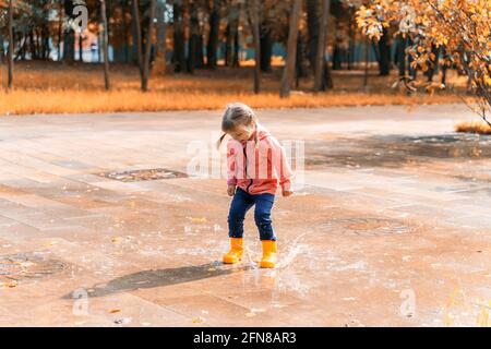 Kind springt und spielt in einer Pfütze nach dem Regen Ein sonniger Herbsttag Stockfoto