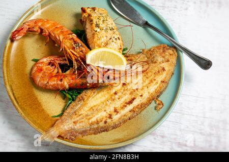 Gemischte Meeresfrüchte auf einem bunten Teller, gibt es gegrillten Lachs, Seezunge, Garnelen und grünen Samphire. Auf einer Scheibe Zitrone. Stockfoto