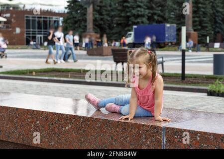Kind Mädchen sitzt auf dem Rand des Brunnens und Blick auf das Wasser Stockfoto