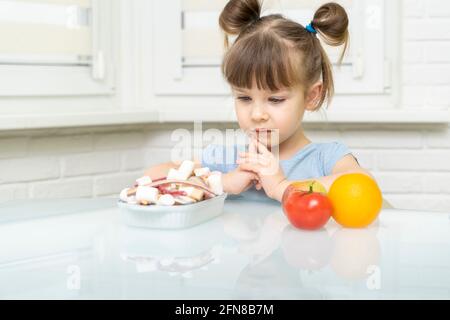 Zuckersucht. Das Kind wählt zwischen süßen Bonbons und gesundem Gemüse und Obst Stockfoto