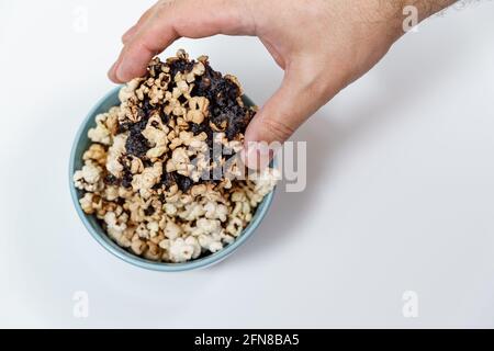 Verbrannter Popcornkern in blauer Tasse, Menschenhand nimmt Popcorn Stockfoto