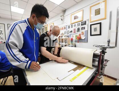 (210515) -- PEKING, 15. Mai 2021 (Xinhua) -- Wang Kun führt einen Schüler dazu, Gravurgemälde an der Pekinger Jianxiang Spezialerziehungsschule in Peking, der Hauptstadt Chinas, zu machen, 13. Mai 2021. Wang Kun, 47, ist eine hörgeschädigte Kunstlehrerin an der Pekinger Jianxiang Spezialerziehungsschule. Die Arbeit als Speziallehrerin war eine Herausforderung. Wang Kun lernt, liest und kommuniziert mit anderen Lehrern, um seine einzigartigen Lehrmethoden zu etablieren. „im Unterricht verwende ich meist anschauliche Beispiele und Vergleiche, um komplizierte Kunsttheorien zu erklären. Gleichzeitig würde ich Bücher und empfehlen Stockfoto