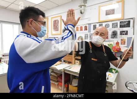 (210515) -- PEKING, 15. Mai 2021 (Xinhua) -- Wang Kun (R) hat sich mit seinem Schüler nach Abschluss eines Kunstwerks an der Pekinger Jianxiang Spezialerziehungsschule in Peking, der Hauptstadt von China, am 13. Mai 2021 hochgestellt. Wang Kun, 47, ist eine hörgeschädigte Kunstlehrerin an der Pekinger Jianxiang Spezialerziehungsschule. Die Arbeit als Speziallehrerin war eine Herausforderung. Wang Kun lernt, liest und kommuniziert mit anderen Lehrern, um seine einzigartigen Lehrmethoden zu etablieren. „im Unterricht verwende ich meist anschauliche Beispiele und Vergleiche, um komplizierte Kunsttheorien zu erklären. Gleichzeitig würde ich es rec Stockfoto