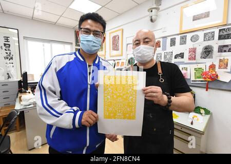 (210515) -- PEKING, 15. Mai 2021 (Xinhua) -- Wang Kun (R) zeigt ein Gravurgemälde, das von seinem Schüler an der Pekinger Jianxiang Spezialerziehungsschule in Peking, der Hauptstadt Chinas, am 13. Mai 2021 erstellt wurde. Wang Kun, 47, ist eine hörgeschädigte Kunstlehrerin an der Pekinger Jianxiang Spezialerziehungsschule. Die Arbeit als Speziallehrerin war eine Herausforderung. Wang Kun lernt, liest und kommuniziert mit anderen Lehrern, um seine einzigartigen Lehrmethoden zu etablieren. „im Unterricht verwende ich meist anschauliche Beispiele und Vergleiche, um komplizierte Kunsttheorien zu erklären. Gleichzeitig würde ich es empfehlen Stockfoto