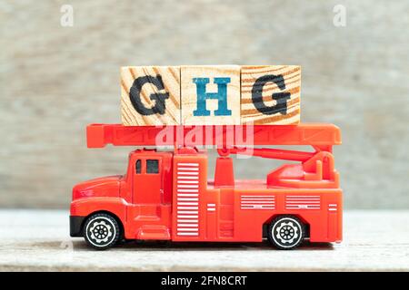 Feuerwehrwagen halten Buchstabenblock in Wort GHG (Abkürzung für Treibhausgas) auf Holzhintergrund Stockfoto