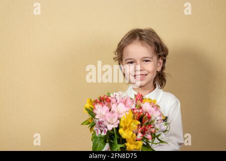 Lächelnd hübscher Junge hält einen Strauß von bunten Blumen auf gelbem Hintergrund. Glückliches Kind gibt einen Strauß von bunten Alstroemeria. Stockfoto