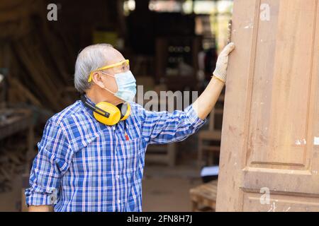 Ältere Arbeiter Holzholzarbeiten Ruhestand Hobby für einen guten Ruhestand, asiatische männliche reifen professionellen Meister der Herstellung von Holzmöbeln mit Gesichtsmaske Protecti Stockfoto