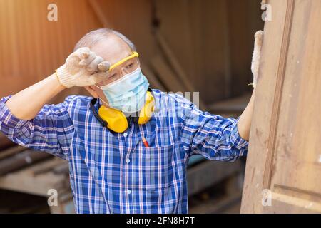 Müde erschöpfte ältere asiatische Arbeit harte Arbeit in heißen Ort wischen Kopf Schweiß Waring Gesichtsmaske für COVID-19 und Staub schützend. Stockfoto