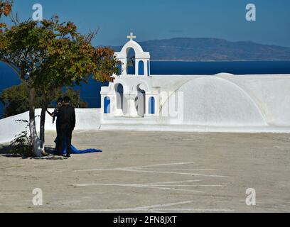 Landschaft mit einem jungen asiatischen Brautpaar vor einer malerischen griechisch-orthodoxen Kapelle auf der Insel Santorin, Kykladen Griechenland. Stockfoto