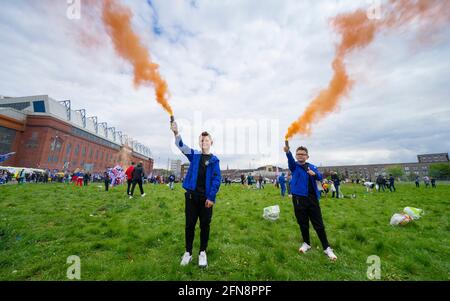 Glasgow, Schottland, Großbritannien. 15 Mai 2021. Tausende von Fans und Fans des Rangers-Fußballvereins kommen im Ibrox Park in Glasgow zusammen, um den Sieg der schottischen Premiership-Meisterschaft zum 55. Mal und zum ersten Mal seit 10 Jahren zu feiern. Rauchbomben und Feuerwerke werden von Fans, die von der Polizei streng kontrolliert werden, weg von den Eingängen des Stadions losgelassen.Pic; Junge Fans mit orangefarbenen Rauchfackeln. Iain Masterton/Alamy Live News Stockfoto