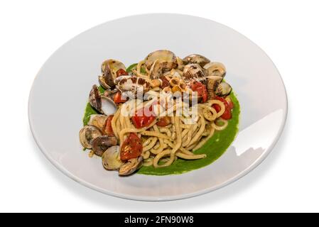 Spaghetti mit Venusmuscheln, Kirschtomaten, Haselnüssen und Gemüsesoße in weißem Teller, isoliert auf Weiß Stockfoto