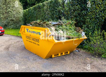 Ein großer, 8 Meter hoher, überfüllter, gelber überlauf, der für die Gartenreinigung und die Beseitigung von Schutt verwendet wurde, voller Gartenabfälle auf einer Fahrt in Surrey, Südostengland Stockfoto