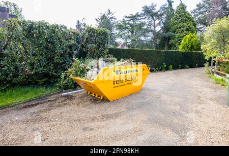 Ein großer, 8 Meter hoher, überfüllter, gelber überlauf, der für die Gartenreinigung und die Beseitigung von Schutt verwendet wurde, voller Gartenabfälle auf einer Fahrt in Surrey, Südostengland Stockfoto