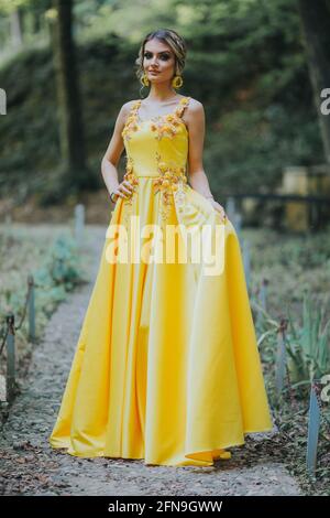 Vertikales Porträt einer wunderschönen kaukasischen blonden Frau, die sie hält Elegantes gelbes Kleid auf der Straße Stockfoto