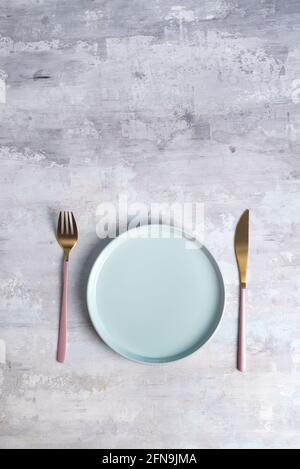 Neues Luxus Golden Besteck mit blauer Platte auf Stein Hintergrund. Draufsicht. Rosafarbenes Messer und Gabel für einen festlichen Tisch für eine Hochzeit, einen Geburtstag oder eine Party. Stockfoto