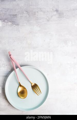 Neues Luxus Golden Besteck mit blauer Platte auf Stein Hintergrund. Draufsicht. Rosafarbenes Messer und Gabel für einen festlichen Tisch für eine Hochzeit, einen Geburtstag oder eine Party. Stockfoto