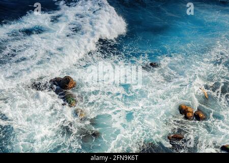 Crushing Meereswellen Textur. Schöne Natur Hintergrund Ansicht von oben. Unglaubliche blaue Farbe des Wassers. Wenige Felsen unter Schaum Stockfoto