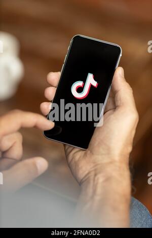 Mann, der ein Smartphone in einem Café hält. TikTok-Logo auf dem Display. Selektiver Fokus. Stockfoto