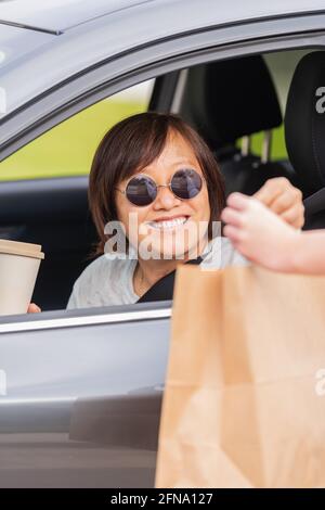 Lächelnde reife asiatische Frau in einem Auto, die ein Papier austauscht Tasche Stockfoto