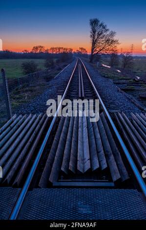 Eisenbahnlinien bei Sonnenuntergang auf der Themse Sümpfe in Lower Higham Kent mit einem aufgehenden Vollmond Stockfoto