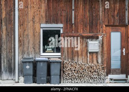 Blick auf ein Haus mit einer hölzernen façade, vor dem sich einige Mülltonnen befinden. Stockfoto