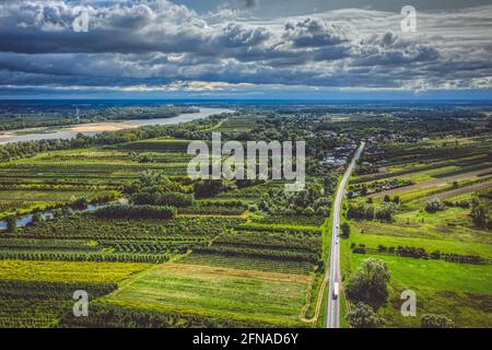 Landschaftlich reizvolle Landschaft, Dorf an gerader Straße und fernem Fluss unter launisch bewölktem Himmel Stockfoto